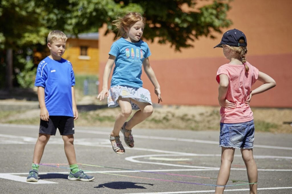 Kinder spielen Gummitwist auf dem Pausenhof der Schule