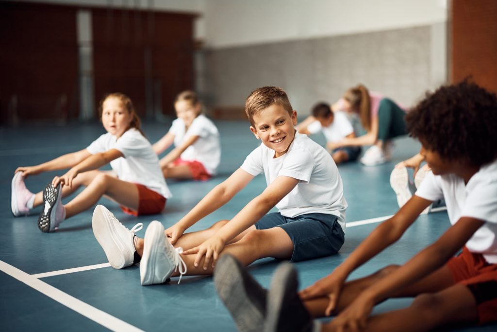 Kinder sitzen auf Turnmatte und dehnen sich