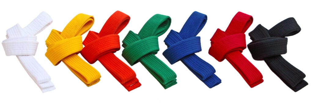 Sieben Karate-Gürtel in Weiß, Gelb, Orange, Grün, Blau, Rot und Schwarz nebeneinander.