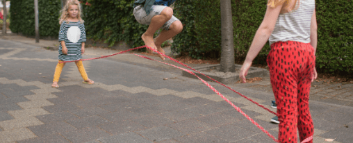 Kinder und Erwachsene spielen mit buntem Gummitwist als Bewegungsspiel im Freien – ideal für Freizeit, Schule und Pausen