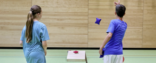 Zwei Schüler spielen in der Turnhalle das Wurfspiel Cornhole