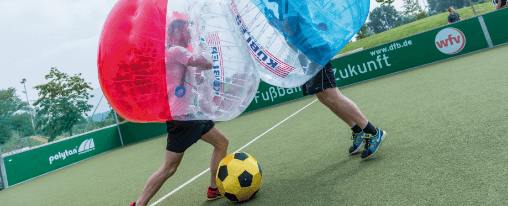 Zwei Männer in Kübler Sport Bubble Soccers mit einem Schaumstoffwürfel in einem Soccer Court