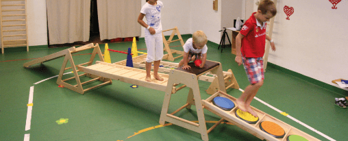 Kinder spielen mit einem Eduygm Bewegungsparcours aus Holz- und Polsterelementen in einer Kita