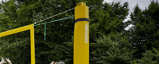 Beachvolleyball-Pfosten auf einem Beachvolleyballfeld mit gespanntem Netz, Court-Lines und Schutzpolstern – geeignet für Teamsport, Training und Wettkampf
