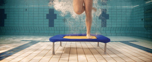 Mehrere Personen springen auf Wassertrampoline im Schwimmbad beim Aquafitness