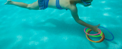 Mehrere bunte Tauchringe liegen am Beckenrand eines Schwimmbads f&uuml;r das Training im Wassersport bereit
