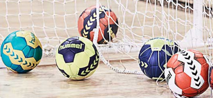Einige Handbälle liegen auf dem Hallenboden in einem Handballtornetz