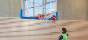 Basketballanlagen kaufen Hängende Basketballanlage in einer Turnhalle, Spieler macht gerade einen Korbleger