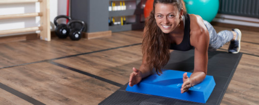 Athletin führt eine Plankübung auf einem Balance Pad und Fitnessmatte in einem Fitnessraum aus