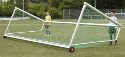 Zwei Spieler bewegen ein auf die Seite geneigtes mobiles Fußballtor mit Hilfe der Angebrachten Transportrollen