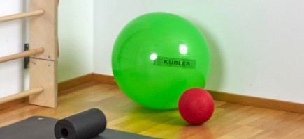 Grüner Sitzball in einer Ecke neben einer Sprossenwand und vor einer Fitnessmatte