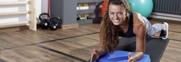 Athletin führt eine Plankübung auf einem Balance Pad und Fitnessmatte in einem Fitnessraum aus