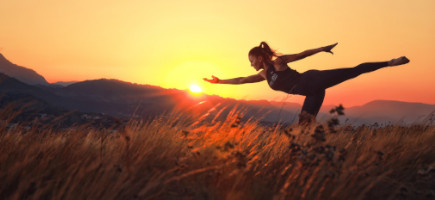 Frau führt Yogaübung auf einer AIREX Matte auf einer Wiese während Sonnenuntergang aus