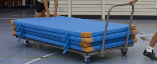 Anordnung vier blauer Kübler Sport Turnmatten aufeinander auf einem Mattenwagen