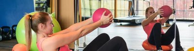 Frau macht im Fitness Übungen mit einem pinken Medizinball