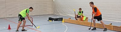 Schüler spielen Hockey in der Turnhalle mit gelben und orangenen Leibchen