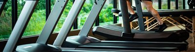 Athlet trainiert auf einem Laufband welches in einer Reihe mit anderen Laufbändern an einem Fenster in einem Fitnessstudio angeordnet ist