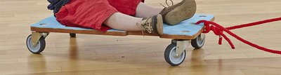 Kind auf einem Kinder Rollbrett aus Holz mit rotem Seil