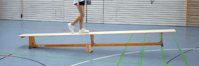 Kind balanciert auf einer schräg gestellten Turnbank in einer Sporthalle