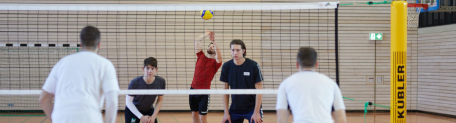 Ein Gruppe Männer spielt in der Turnhalle Volleyball mit einem Kübler Sport Volleyballnetz