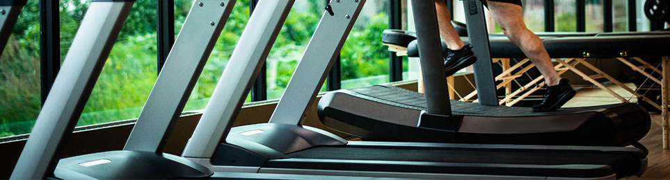 Athlet trainiert auf einem Laufband welches in einer Reihe mit anderen Laufbändern an einem Fenster in einem Fitnessstudio angeordnet ist