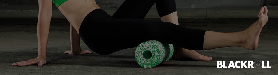 Frau macht Übungen mit einer grünen Blackroll für die Kniekehle