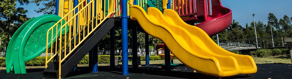 Kinder rutschen auf einer robusten Spielplatzrutsche im Außenbereich eines Spielplatzes