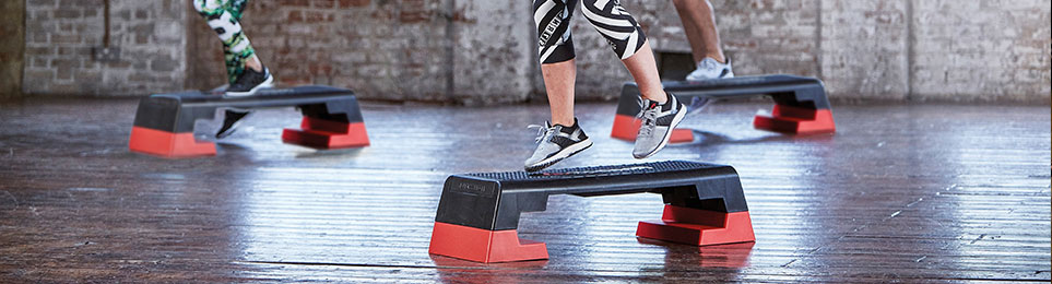 Fitnessgruppe in einem Kursraum trainieren jeweils mit einem Steppbrett