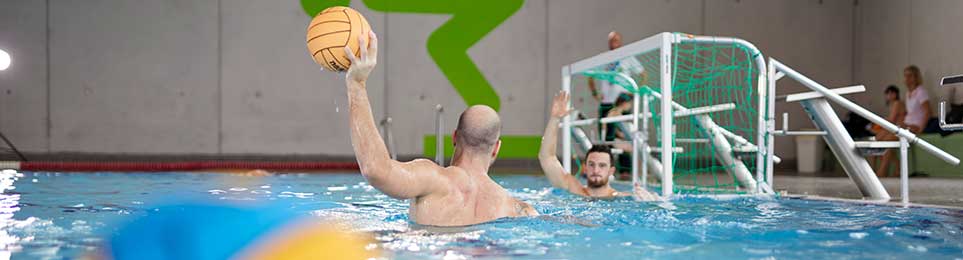 Spielerinnen und Spieler beim Wasserball mit Ball und Tor im Schwimmbecken während eines Wettkampfs