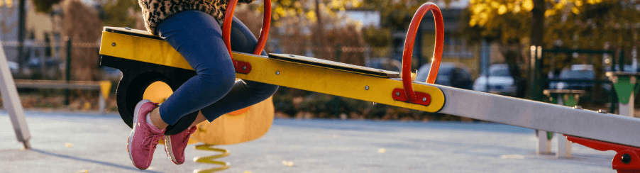 Montierte Balkenwippe aus Metall auf einem modernen Kinderspielplatz mit mehreren Kindern beim Wippen
