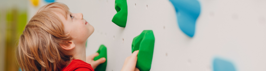 Kind an verschiedenen Klettergriffen an einer Kletterwand in einer modernen Kletterhalle