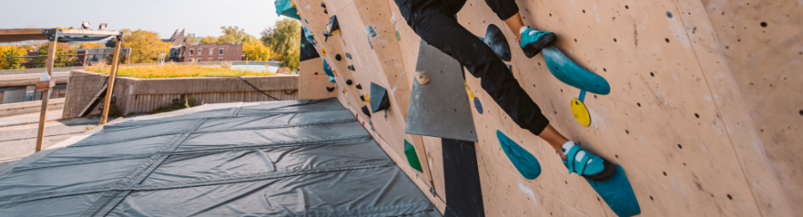 Kletternde Person trägt Kletterschuhe an einer künstlichen Kletterwand