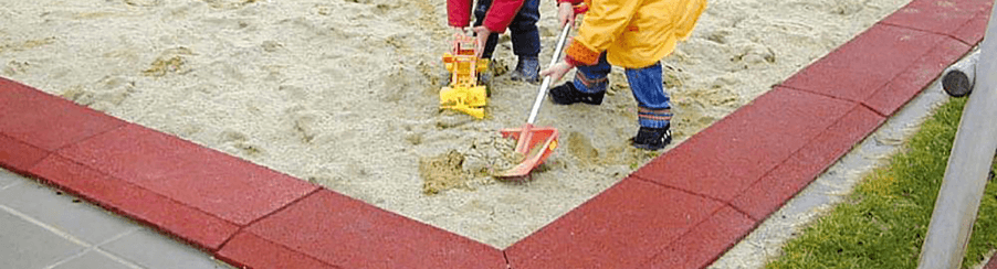 Kinder spielen in einem großen Sandkasten mit Spielturm und Sandspielzeug auf einem Spielplatz