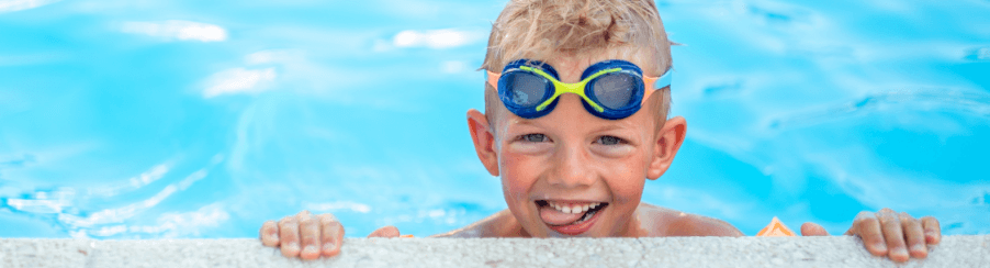 Lächelndes Kind mit Schwimmbrille beim Schwimmen im Hallenbad