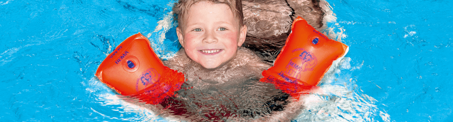 Mehrere bunte Schwimmflügel liegen am Beckenrand eines Schwimmbads