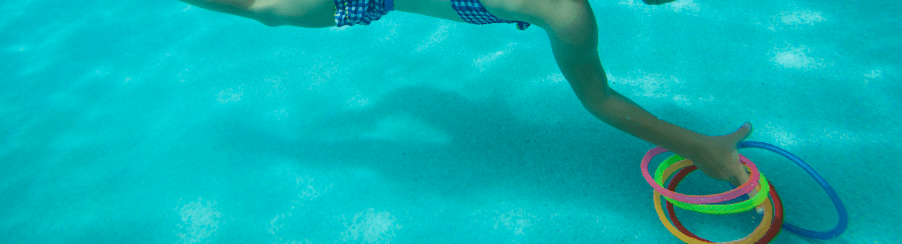 Mehrere bunte Tauchringe liegen am Beckenrand eines Schwimmbads für das Training im Wassersport bereit