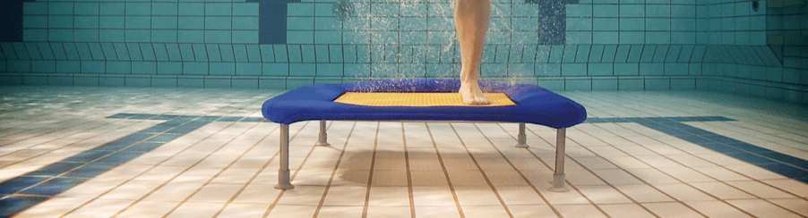 Mehrere Personen springen auf Wassertrampoline im Schwimmbad beim Aquafitness