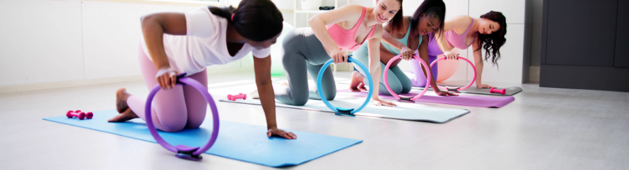 Vier Frauen im Pilates auf einer Fitnessmatte mit jeweils einen bunten Pilates Ring